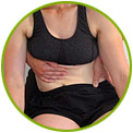 A person wearing a black sports bra receives abdominal support from another persons hands during what appears to be a physical therapy or exercise session.